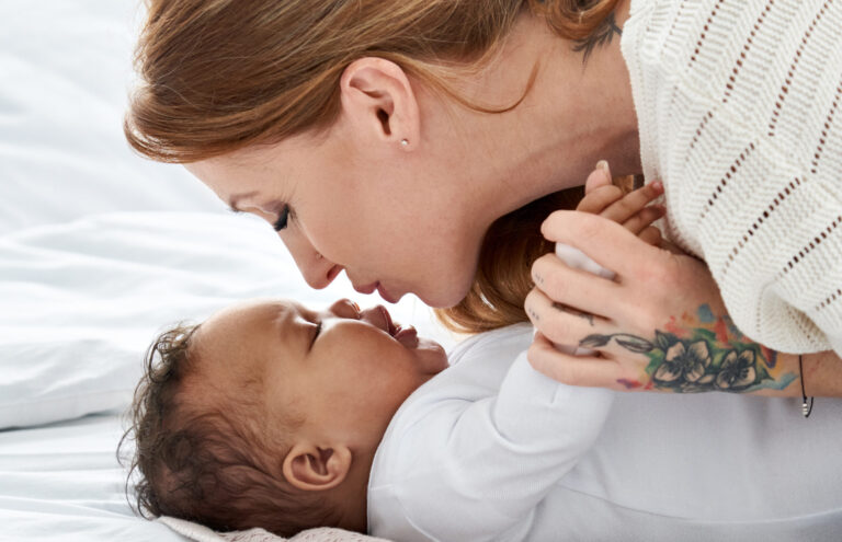 Comment le biberon main libre transforme le quotidien des parents young caucasian mother kissing cute african american baby daughter lying in bed.